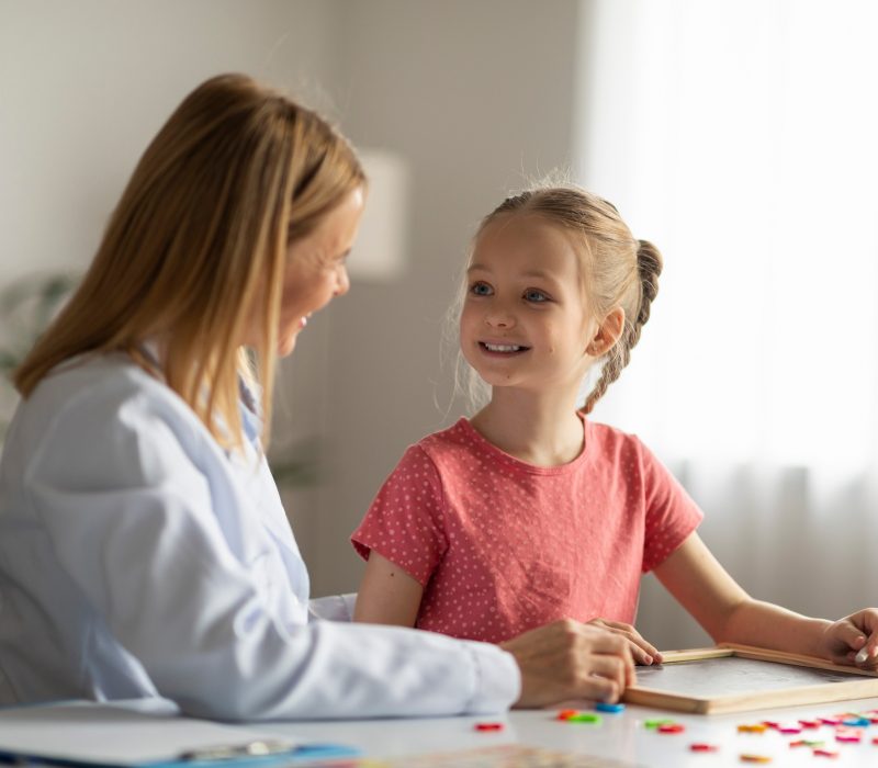 Cute Little Girl Looking At Therapist Lady During Session Meeting In Office