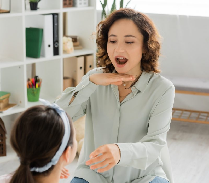 Speech therapist opening mouth and gesturing near blurred pupil in consulting room