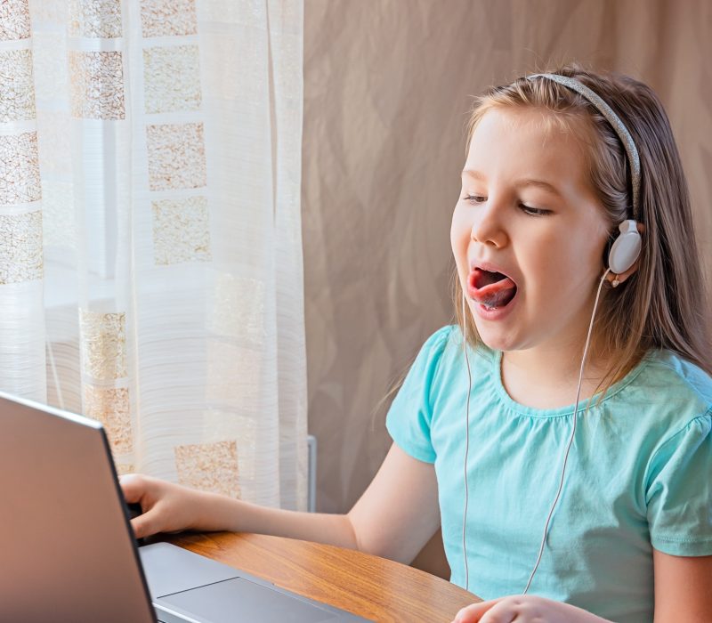 Speech training concept. Little girl uses a laptop to study at home with a teacher, a speech therapi